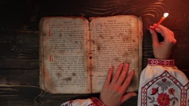 Ukraynalı kadın İncil 'i okuyor. Dikkatli bir şekilde mum ışığı altındaki kağıt sayfaya odaklanmış. Kyiv Rus tarihi. Mezmur, 19. yüzyıl, dualar ve ilahiler. Yüksek 4K görüntü