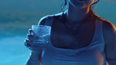 Islak seksi kadın alkol içiyor ve geceleri yüzme havuzunda dans ediyor. Yaz partisi, vücut hareketi, dar beyaz elbiseli kadın. Gece hayatı, kokteyller, yetişkinler için eğlence. 4k görüntü