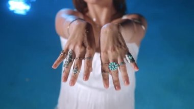Güzel çingene kadın boho mücevherlerini, ellerinde taşlarla yüzüklerini gösteriyor. Mavi sularda aksesuar gösteren beyaz elbiseli bir kız. Kadınlık kavramı. Yüksek kalite 4k görüntü