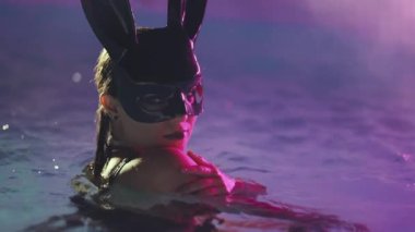 Geceleri havuzda yüzen tavşan lateks maskeli seksi kadın. Siyah mayo giymiş çekici bir piliç parti zamanı eğleniyor. Zengin yaşam tarzı, lüks hayat, eğlence, maskeli balo. Tehlikeli bir kız. 4k görüntü