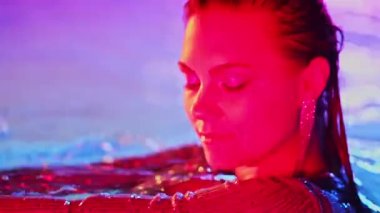 Havuz suyunda neon ışığı altında poz veren güzel bir kadın. Parti, parlak elbiseli çekici piliç gecenin tadını çıkarıyor. Zengin yaşam tarzı, lüks yaşam, nüfuzlu insanlar. Yüksek kalite 4k görüntü