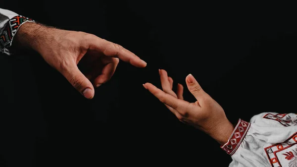 Idea of earth creation. Ukrainian hands reaching out, pointing finger together on black background. Man and woman in embroidered shirts, love, religion. Contemporary art, evolution, origins concept