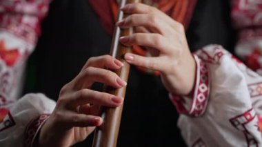 Tahta flüt çalan kadının elleri. Karanlık arka planda Ukrayna sopilkası. Halk müziği konsepti. Müzik aleti. Geleneksel nakışlı gömlekli müzisyen Vyshyvanka. 4k görüntü