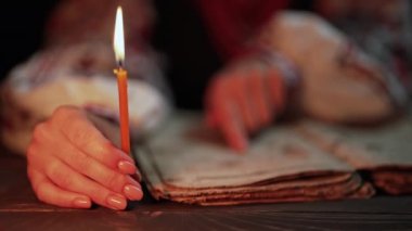 Ukraynalı kadın İncil 'i okuyor. Dikkatli bir şekilde mum ışığı altındaki kağıt sayfaya odaklanmış. Kyiv Rus tarihi. Mezmur, 19. yüzyıl, dualar ve ilahiler. Yüksek 4K görüntü