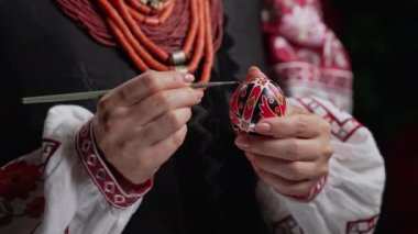 Paskalya yumurtasına geleneksel orisim çizen Ukraynalı kadın: Pysanka. Ulusal kostümle çalışan bir sanatçı. Hristiyan bayramı için hazırlık. Yüksek kalite 4k görüntü