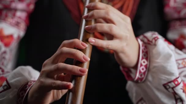 木管楽器のフルートで演奏する女性の手 暗い背景にウクライナのソフィルカ 民俗音楽の概念 伝統的な刺繍シャツのミュージシャン Vyshyvanka 4K映像 — ストック動画
