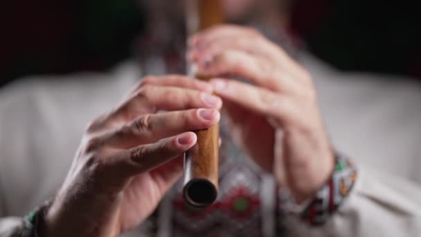 木管楽器のフルートで演奏する男の手 暗い背景にウクライナのソフィルカ 民俗音楽の概念 伝統的な刺繍シャツのミュージシャン Vyshyvanka 高4K映像 — ストック動画