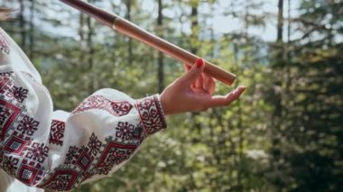 Tahta flüt çalan kadının eli - Ukraynalı pembe dizi ya da orman arka planında Tylynka. Halk müziği konsepti. Müzik aleti. Geleneksel nakışlı gömlekli müzisyen Vyshyvanka. 4k