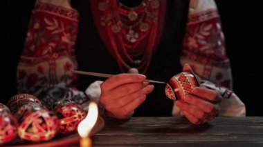 Paskalya yumurtasına geleneksel orisim çizen Ukraynalı kadın: Pysanka. Ulusal kostümle mum ışığında çalışan bir sanatçı. Hristiyan bayramı için hazırlık. Yüksek kalite 4k görüntü