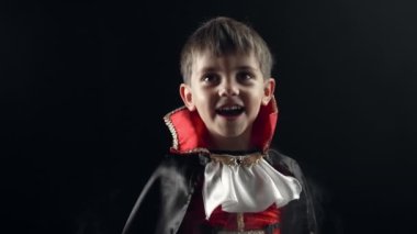 Vampir Dracula kostümlü mutlu küçük çocuk gülümsüyor, dumanlı renkli arka planda samimi bir şekilde seviniyor. Cadılar Bayramı, şeker mi şaka mı, parti dekorasyonu konsepti. Yüksek kalite 4k görüntü