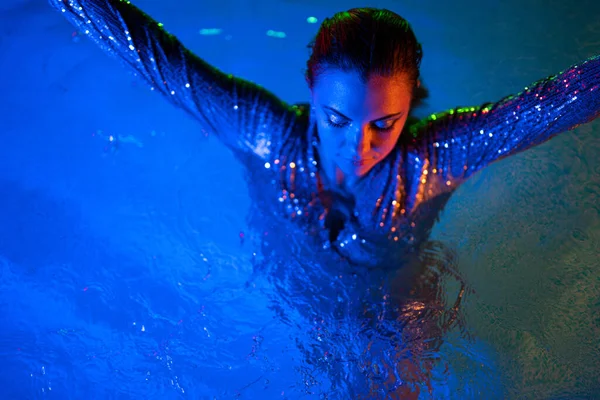 ネオンカラーの光の下でプールの水の中でグラマラスセクシーな女性 パーティー 夜の時間を楽しんでドレスを輝いて魅力的な女の子 モデル インフルエンサーとして働く 高品質の写真 — ストック写真