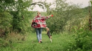 Güzel yeşil bahçede köpek yavrusuyla koşan bir kadın. Sahibi köpek tasmasını takıyor, trenleri yakın tutuyor. Sevimli bir hayvan, ailenin yeni üyesi. Yüksek kalite 4k görüntü
