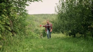 Güzel yeşil bahçede köpek yavrusuyla koşan bir kadın. Sahibi köpek tasmasını takıyor, trenleri yakın tutuyor. Sevimli bir hayvan, ailenin yeni üyesi. Yüksek kalite 4k görüntü