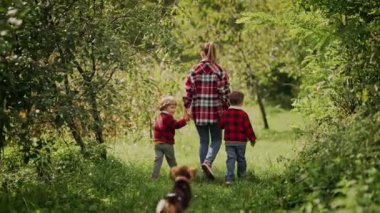 Genç bir aile, anne ve iki erkek kardeş ikiz erkek kardeş yeşil parkta ya da bahçede köpek yavrusuyla koşuyorlar. Mutlu anne ve çocuklar, aşk, özgürlük, gelecek konsepti. Yüksek kalite 4k görüntü