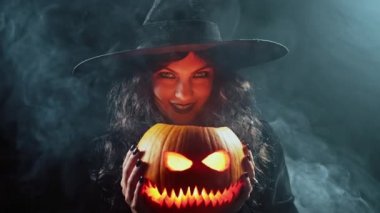 Karanlık arka planda balkabağı buharı üstünde balkabağı olan gizemli kara cadı. Cadılar Bayramı 'nın korkunç sembolü, maskeli balo kostümü, parti dekorasyonu. Sihir, klasik cadı. Yüksek kalite 4k görüntü