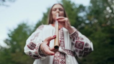 Tahta flüt çalan kadının eli - Ukraynalı pembe dizi ya da orman arka planında Tylynka. Halk müziği konsepti. Müzik aleti. Geleneksel nakışlı gömlekli müzisyen - Vyshyvanka 4k