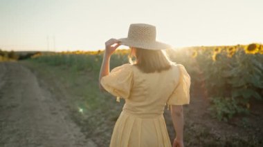 Tanımlanamayan bir kadın, retro elbiseli, ayçiçeği tarlasının yakınında tek başına yürüyor. Klasik moda, inanılmaz macera, kırsal alan, kırsal alan, doğal yaşam tarzı. Yüksek kalite 4k görüntü