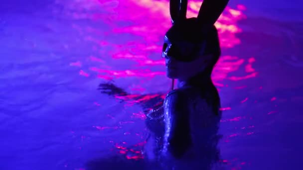 夜に水の中で泳ぐウサギのラテックスマスクの魅力的な女性 パーティーの時間を楽しんで輝くドレスで魅力的な女の子 豊かなライフスタイル 豪華な生活 エンターテイメント 仮面舞踏会 高品質4K映像 — ストック動画