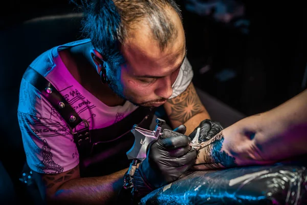 Portrait of man tattoo master with dreadlocks showing process of creation tattoo on female body under lamp light. Professional artist working in salon. High quality photo