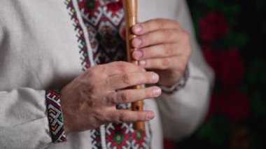 Tahta flüt çalan adamın elleri. Karanlık arka planda Ukrayna sopilkası. Halk müziği konsepti. Müzik aleti. Geleneksel nakışlı gömlekli müzisyen Vyshyvanka. Yüksek 4K görüntü