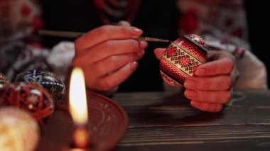 Paskalya yumurtasına geleneksel orisim çizen Ukraynalı kadın: Pysanka. Ulusal kostümle mum ışığında çalışan bir sanatçı. Hristiyan bayramı için hazırlık. Yüksek kalite 4k görüntü