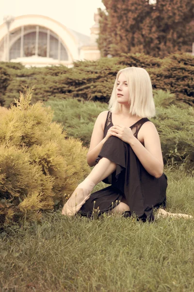 Ballerina in pointe sitting on the grass — Stock Photo, Image