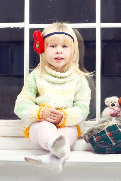 Klein meisje in gebreide trui op het venster — Stockfoto