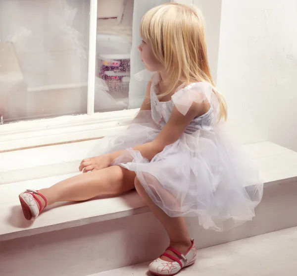 Menina 3 anos de idade em um vestido branco perto da janela — Fotografia de Stock