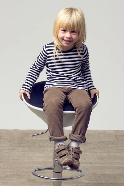 Meisje 3 jaar oud in spijkerbroek zit op een hoge stoel — Stockfoto