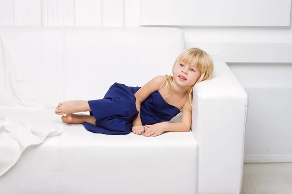 Dziewczyna jest w niebieską sukienkę na białej kanapie — Zdjęcie stockowe