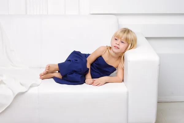 Meisje is in blauwe jurk op een witte sofa — Stockfoto