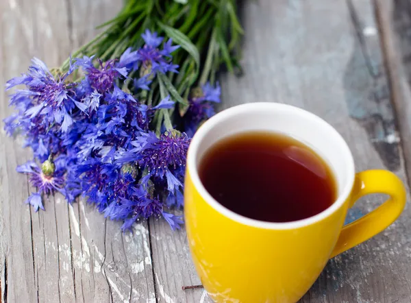 Gelbe Tasse Tee und ein Strauß Kornblumen — Stockfoto