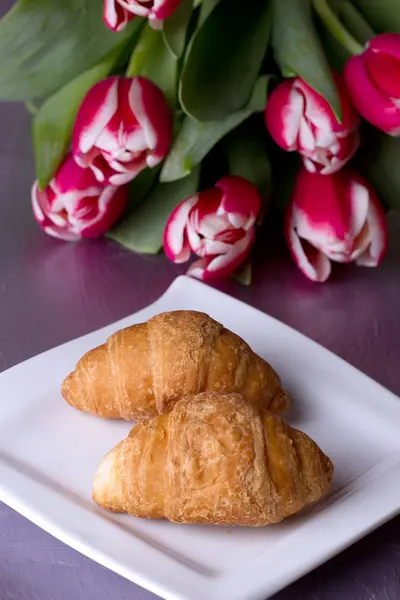 Zwei Croissants neben einem Strauß Tulpen — Stockfoto