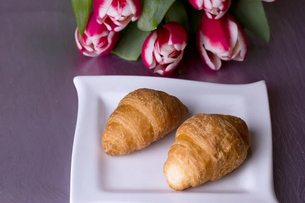 Two croissants next to a bouquet of tulips — Stock Photo, Image