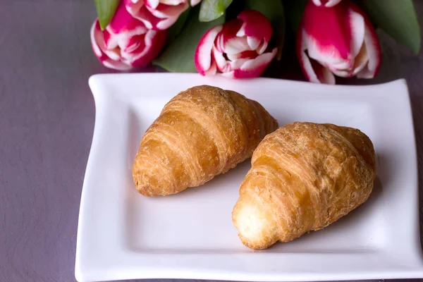 Two croissants next to a bouquet of tulips — Stock Photo, Image