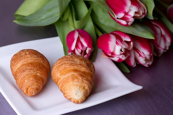 Two croissants next to a bouquet of tulips — Stock Photo, Image