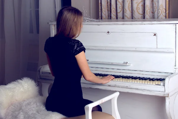 Flicka i svart klänning spelar på en vit piano — Stockfoto