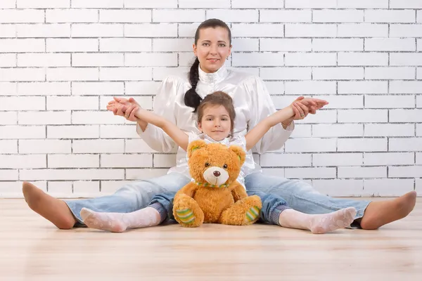 Mother, daughter and toy sitting against the wall — Stock Photo, Image