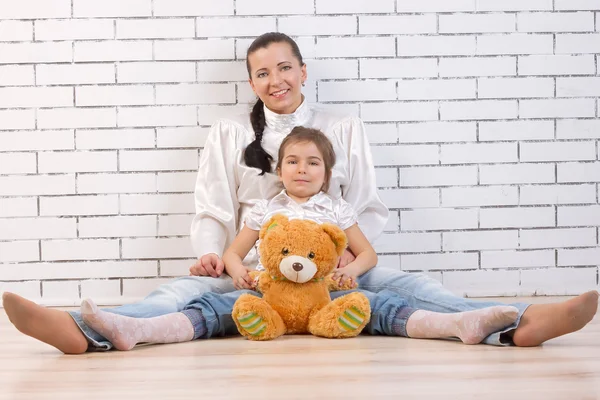 Mother, daughter sitting near a white wall — Stock Photo, Image
