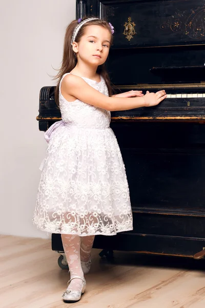 Menina em um vestido preto fica perto do piano — Fotografia de Stock