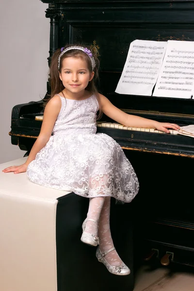 Girl in a black dress sitting near the piano — Stok fotoğraf