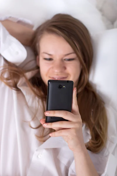 Happy girl reading on the phone while — Stock Photo, Image
