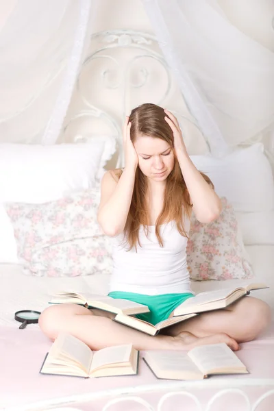 Meisje op het bed, omringd door boeken — Stockfoto