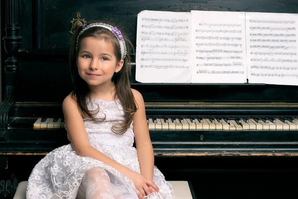 Cute 5 year old girl sitting by piano — Stock Photo, Image