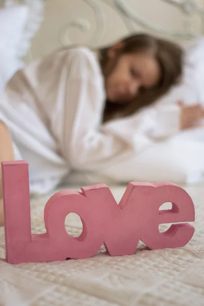 Palavra amor em uma cama ao lado da menina — Fotografia de Stock