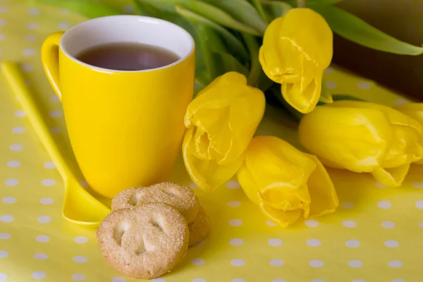 Tazza gialla di tè accanto a tulipani e biscotti — Foto Stock