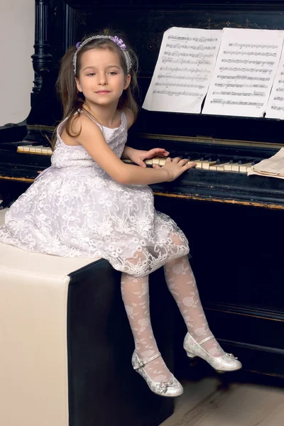 Meisje in een mooie jurk zit aan de piano — Stockfoto