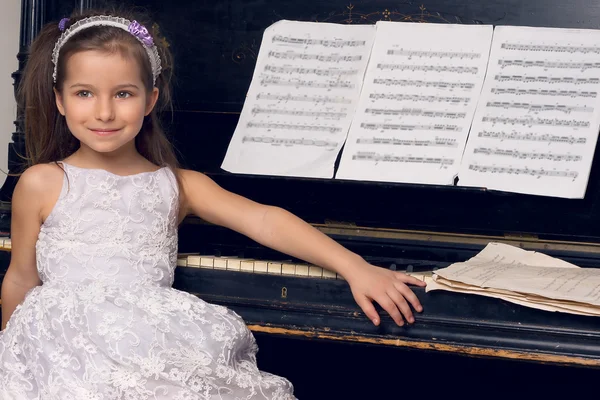 Dívka v krásných šatech sedí u klavíru — Stock fotografie
