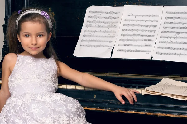 Meisje in een mooie jurk zit aan de piano — Stockfoto