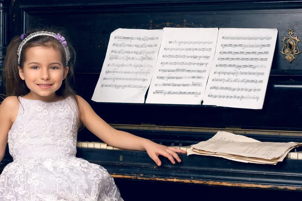 Chica en un hermoso vestido se sienta al piano — Foto de Stock